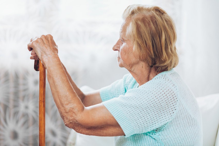 senior woman sitting with both hands on walking stick