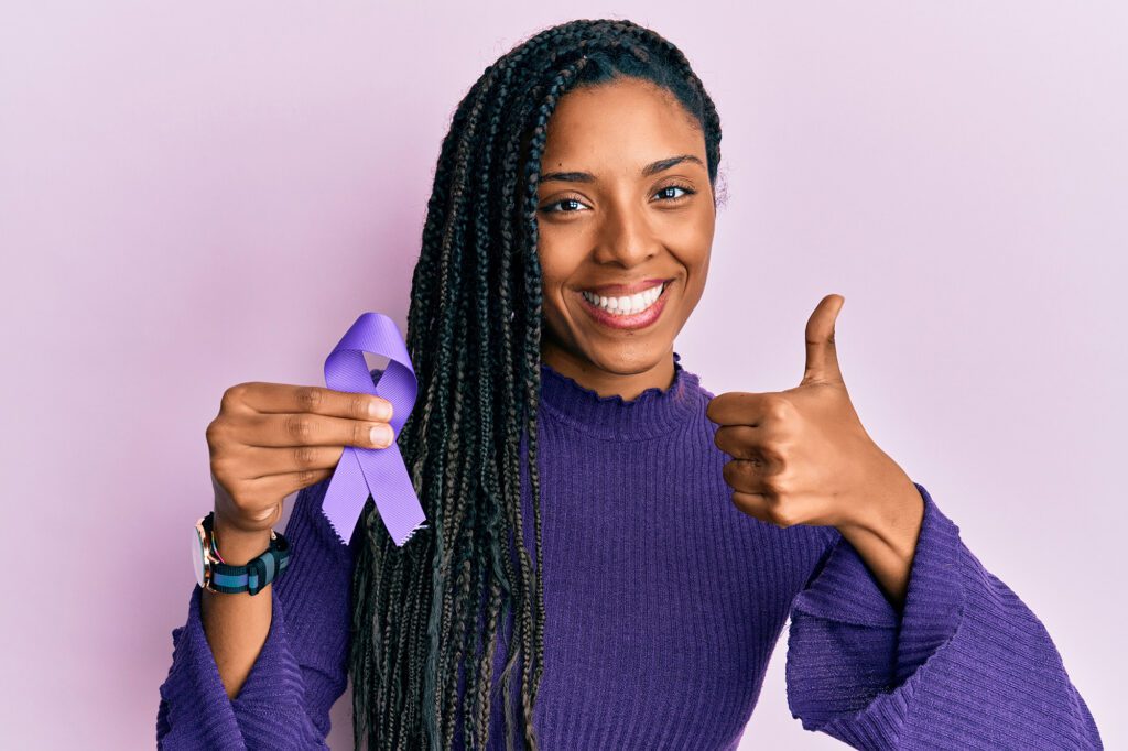 black woman holding lupus awareness ribbon while smiling and giving a thumbs up gesture