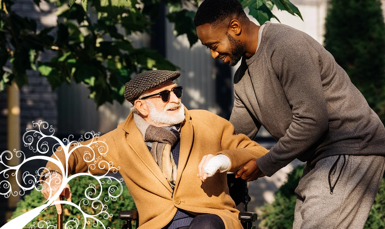 A young man smiles warmly as he helps an elderly man in a wheelchair. The older man, in a brown coat and cap, looks content. Sunlight filters through trees.
