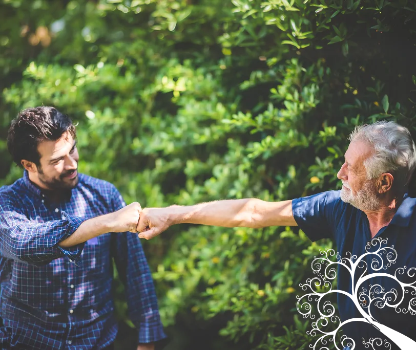 Young caregiver and senior man greeting each other with a friendly fist bump outdoors.