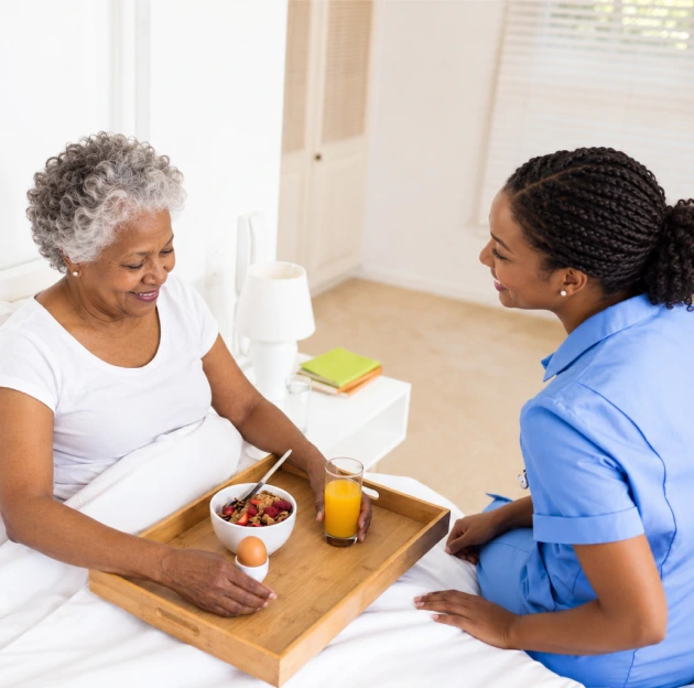 Caregiver supporting an older woman with her meal and daily routine